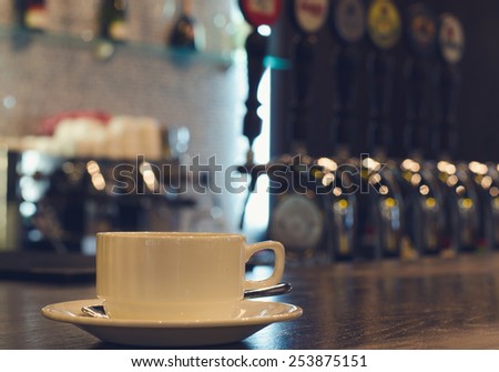 Coffee cup and saucer standing on a wooden counter in a bar with a view to the beer taps in the background