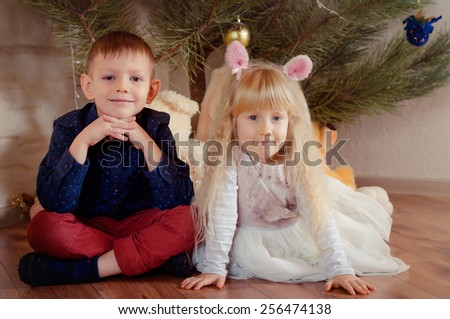 Cute happy little boy and pretty blond girl wearing a set of pink ears on a headband sitting side by side on the floor looking at the camera with charming friendly smiles