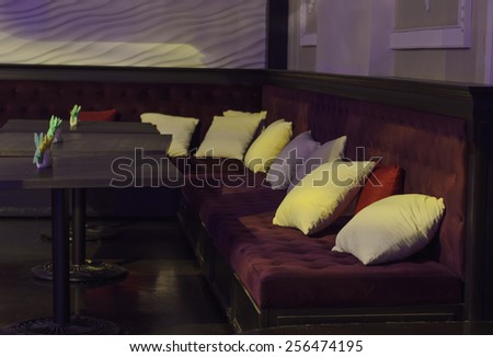 Empty tables and comfortable upholstered benches with cushions in a bar or nightclub in dim light