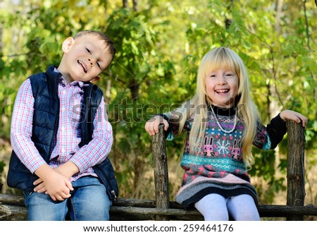 Happy Little Young Kids in an Autumn Style Outfits Sitting on the Wooden Garden Fence.