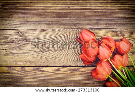 Bouquet of delicate fresh red tulips lying on a wood textured background with wood grain pattern and copyspace for a Valentines Day card