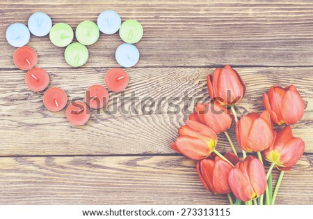 Bunch of fresh red tulips lying alongside a a heart formed of colorful candles for a loved one or sweetheart on Valentines Day or an anniversary, overhead view