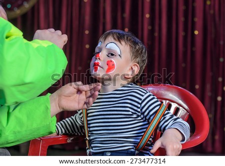 Cute Young Boy Sitting on a Chair, Applied with Makeup by an Artist to Look Like a Mime for a Stage Play.