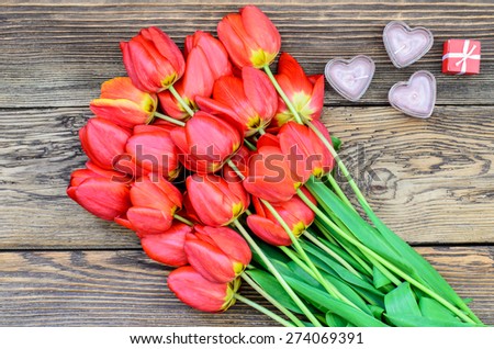 Bunch of fresh red tulips lying alongside a a heart candles for a loved one or sweetheart on Valentines Day or an anniversary, overhead view