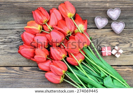 Bunch of fresh red tulips lying alongside a a heart candles for a loved one or sweetheart on Valentines Day or an anniversary, overhead view