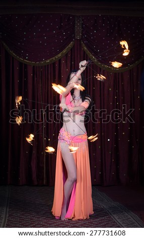Portrait of Fire Dancer Performing with Flaming Fire Hoop Above Head on Dark Background