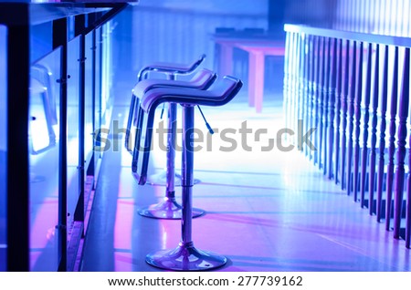 Profile of Empty Bar Stools Along Bar Illuminated in Purple Light at Night Club
