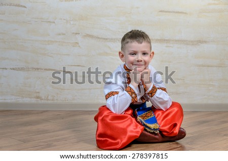 Cute young boy sitting on a wooden floor in a colorful dance or pantomime costume scratching his head and thinking with a puzzled expression