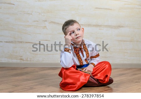Cute young boy sitting on a wooden floor in a colorful dance or pantomime costume scratching his head and thinking with a puzzled expression