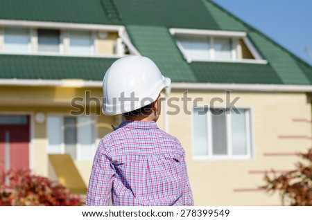 Rear View of Young Boy Wearing Plaid Shirt and White Hard Hat Standing on Steps in front of House as if Admiring Work or Monitoring Job Site