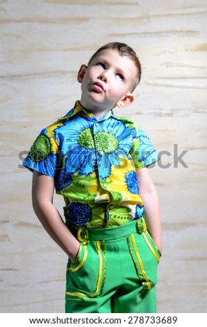 Cute little boy in colorful clothes standing thinking staring up into the air with a contemplative expression and his hands in his pockets