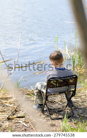 Young Boy Sitting on a Chair at the Riverside, Holding his Fishing Rod While Catching Fish at the River.