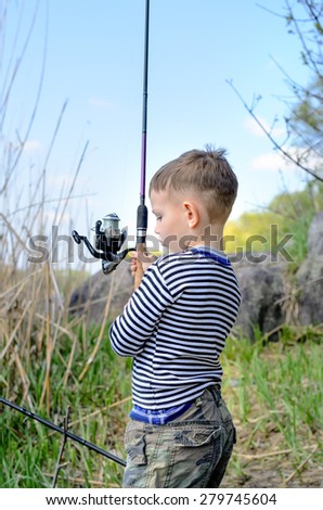 Young boy holding up his fishing rod and spinning reel as he prepares to cast in from a lake shore