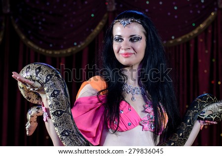 Close Up of Exotic Female Snake Dancer with Dark Hair Holding Large Snake in Both Hands Standing on Stage