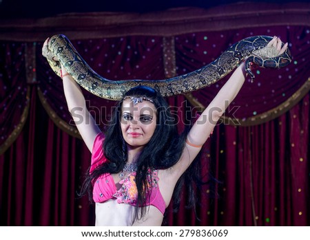 Close Up of Exotic Female Snake Dancer with Dark Hair Holding Large Snake in Both Hands Standing on Stage