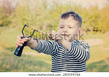 Waist Up of Young Boy Wearing Striped Shirt Holding Sling Shot with Rubber Bands Pulled Back in Anticipation of Catapulting Projectile