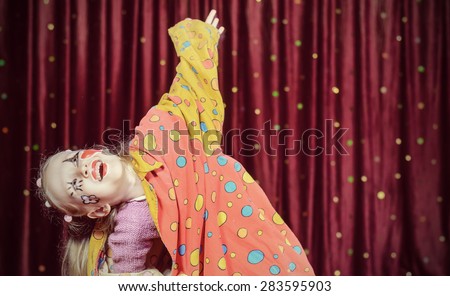 Young Blond Girl Wearing Clown Make Up and Polka Dot Costume Shielding Eyes from Bright Stage Lights in front of Red Curtain