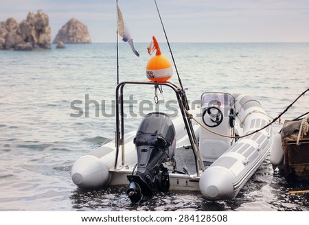 Rear View of Small Inflatable Fishing Boat Tied Up at Dock with View of Rocky Islands in Ocean Under Overcast Sky