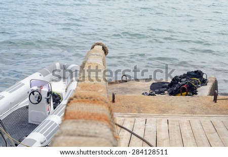 Small Fishing Boat Tied Up Next to Dock with Pile of Scuba Diving Equipment Drying in Sun, with Perspective View Down Railing