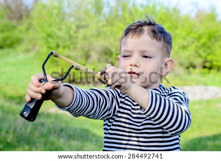 Waist Up of Young Boy Wearing Striped Shirt Holding Sling Shot with Rubber Bands Pulled Back in Anticipation of Catapulting Projectile