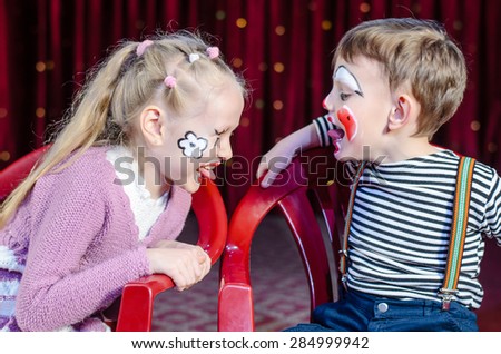 Boy and Girl Wearing Clown Make Up Sitting Side by Side and Sticking Tongues Out at Each Other