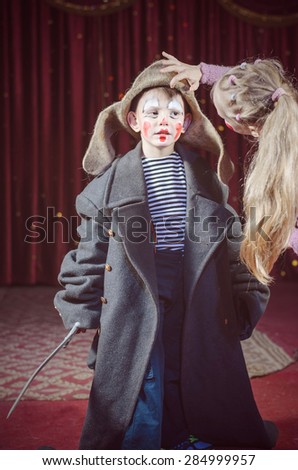 Girl Adjusting Floppy Hat of Boy Wearing Pirate Clown Make Up and Over Sized Grey Coat Holding Toy Prop Sword