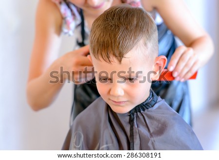 Hairdresser cutting a young boys hair with an electric razor trimming the side into a short hairstyle, close up view