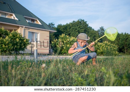Portrait of Serious Young Boy with Bug Net Crouching in Long Grass on Lawn Outdoors in Summer
