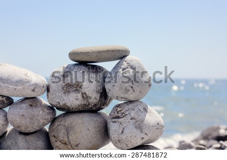 Small Flat Rock Balancing on Top of Small Rock Wall on Beach with Sparkling Ocean Water in Background