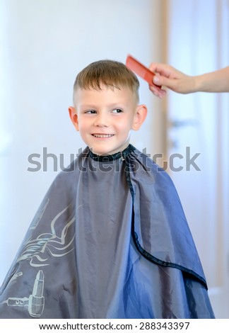Smiling little boy having his hair cut into a short hairstyle by a hairdresser in her salon