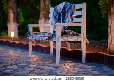 Inviting White Bench Covered in Plaid Blankets on Stone Patio Illuminated in Soft Light at Dusk