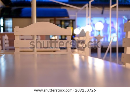 White Tables and Chairs on Outdoor Patio at Night, View of Empty Restaurant or Club Patio from Across Shiny Clean Table Surface