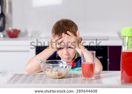 Little boy sitting at the kitchen table eating looking at his food in horror with his head resting on his hands