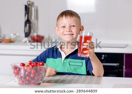 Portrait of Smiling Young Boy Drinking Glass of Red Juice While Sitting at Table with Bowl of Cherries in Kitchen