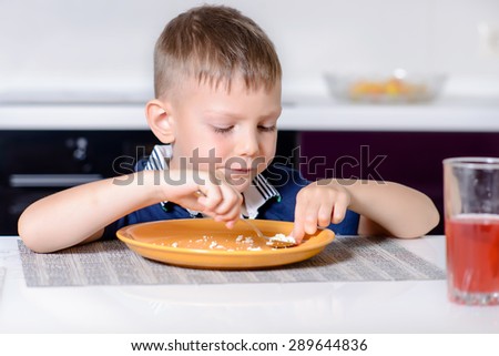 Young Blond Boy Eating Last Bite of Food from Plate While Sitting at Kitchen Table