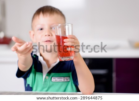 Young Blond Boy Smiling and Holding Glass of Red Juice Up Toward Camera and Smiling