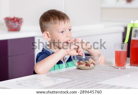 Young Boy Having Breakfast at Kitchen Table, Enjoying Bowl of Oatmeal Cereal with Cherries on Top and Glass of Red Juice