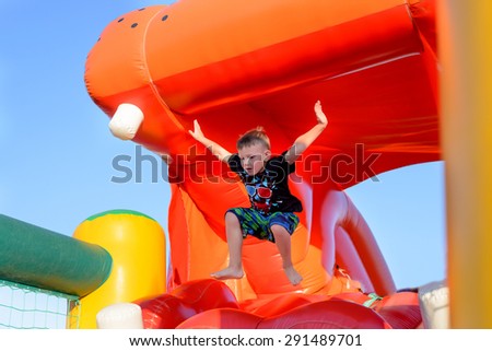Young boy jumping barefoot on a plastic jumping castle with his arms in the air as he enjoys a summer day at a playground or fair