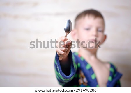 Young boy holding out a metal kitchen spoon towards the camera in his hand with focus to the utensil, copyspace to the side