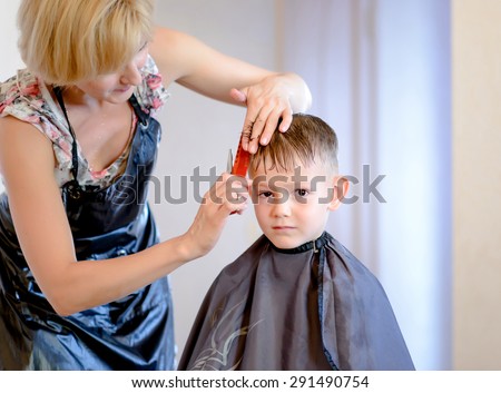 Hairdresser cutting a little boys hair into a short hairstyle in her salon
