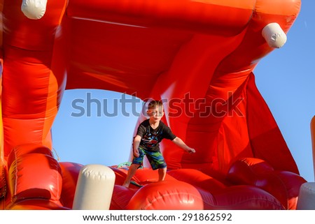 Waist up of blond boy (7-9 years) wearing black t-shirt with colorful print playing in red bouncy castle
