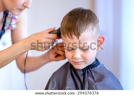 Handsome little boy getting a hair cut using an electric razor in a hair salon, closeup of his face and the hands of the hairdresser