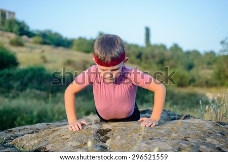 Sporty Young Boy Doing Push up Exercise on Top of a Boulder on a Sunny Day Against Blurry Nature Background.