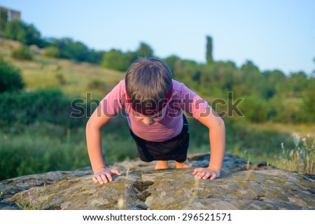 Sporty Young Boy Doing Push up Exercise on Top of a Boulder on a Sunny Day Against Blurry Nature Background.