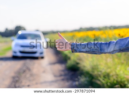 Young woman hitchhiking in the countryside flagging doan an approaching car on a farm road with her thumb
