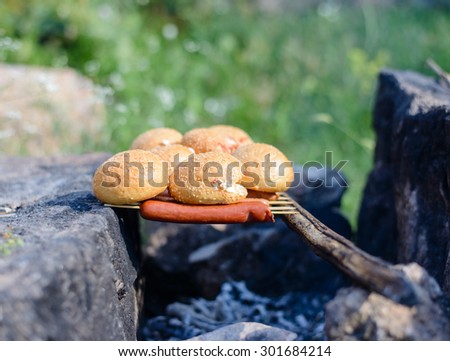 Cooking over a makeshift campfire with sausages on skewers and fresh bread rolls balanced on a stick over the coals
