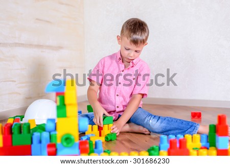 Young boy playing with colorful building blocks creating a robot and train engine turning to smile at the camera