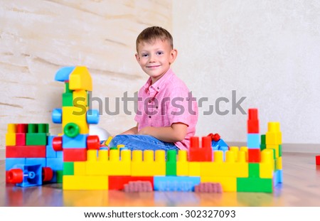 Young boy playing with colorful building blocks creating a robot and train engine turning to smile at the camera