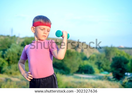 Smiling Strong Cute Boy Lifting Dumbbell with his Right Hand on his Waist While Doing an Outdoor Exercise
