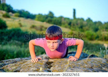 Athletic Young Boy Forcing his Body to Lift While Doing Push Up Exercise on Top of a Big Rock with Sacrificing Facial Expression.